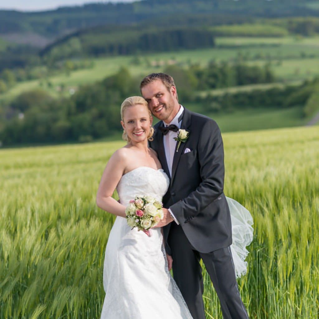 Das glückliche Brautpaar einer Hochzeit im Romantik Hotel Platte auf einem Feld.