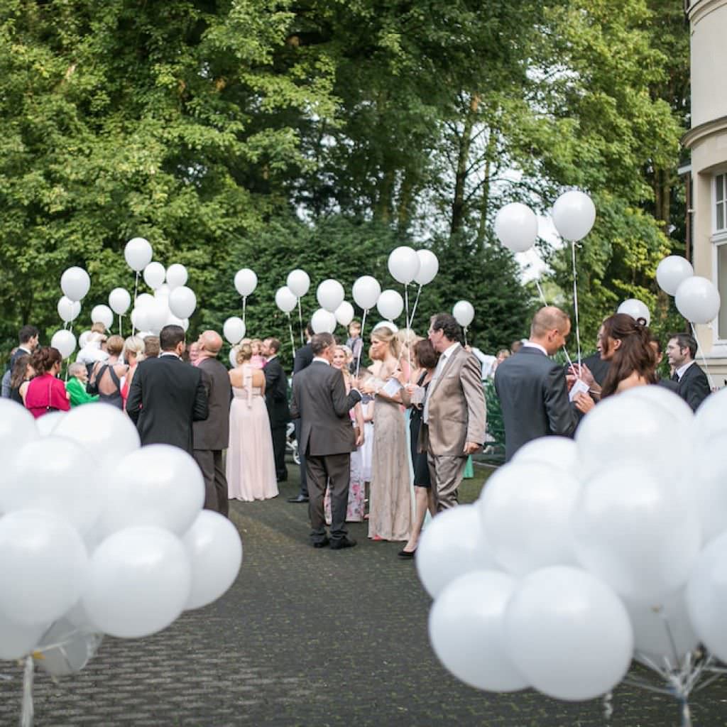 Gäste einer Hochzeit in der Bayer Villa empfangen das Brautpaar mit weißen Luftballons.