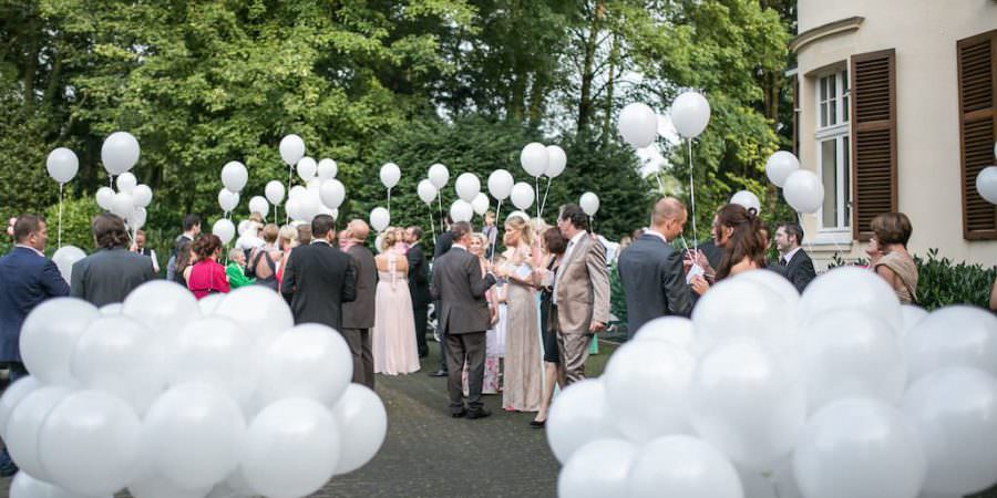 Gäste einer Hochzeit in der Bayer Villa empfangen das Brautpaar mit weißen Luftballons.