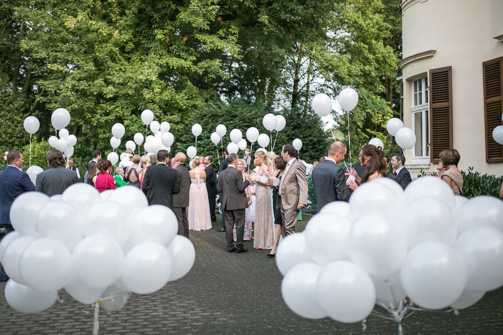 Gäste einer Hochzeit in der Bayer Villa empfangen das Brautpaar mit weißen Luftballons.