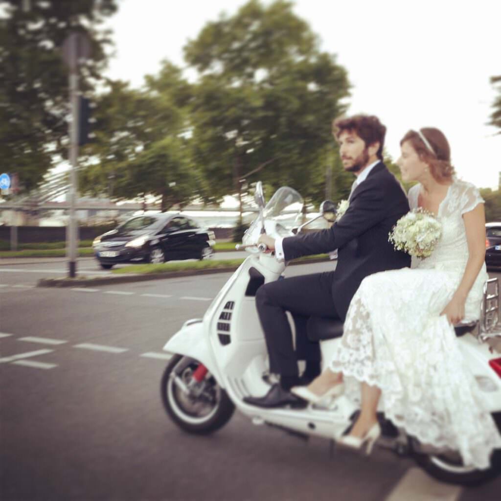 Das Brautpaar einer deutsch-französischen Hochzeit in den Rheinterrassen kommt auf einer Vespa an.