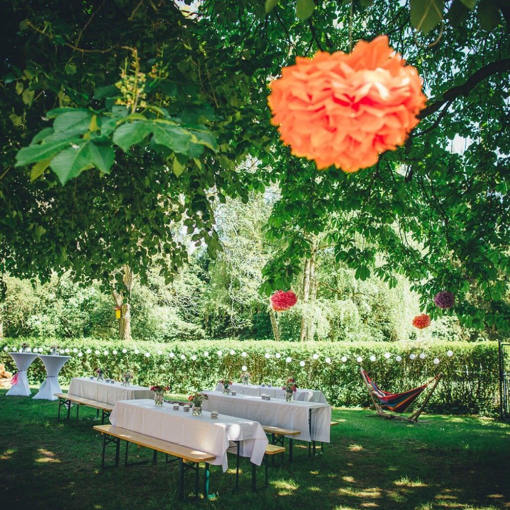 Gedeckte Gartentische und bunte Pompoms bei einer Sommerhochzeit auf dem Bauernhof.