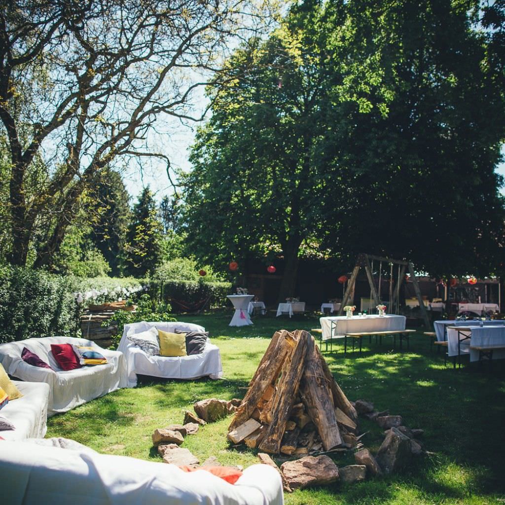 Gemütliche Sofas mit bunten Kissen am Lagerfeuer bei einer Sommerhochzeit auf dem Bauernhof.