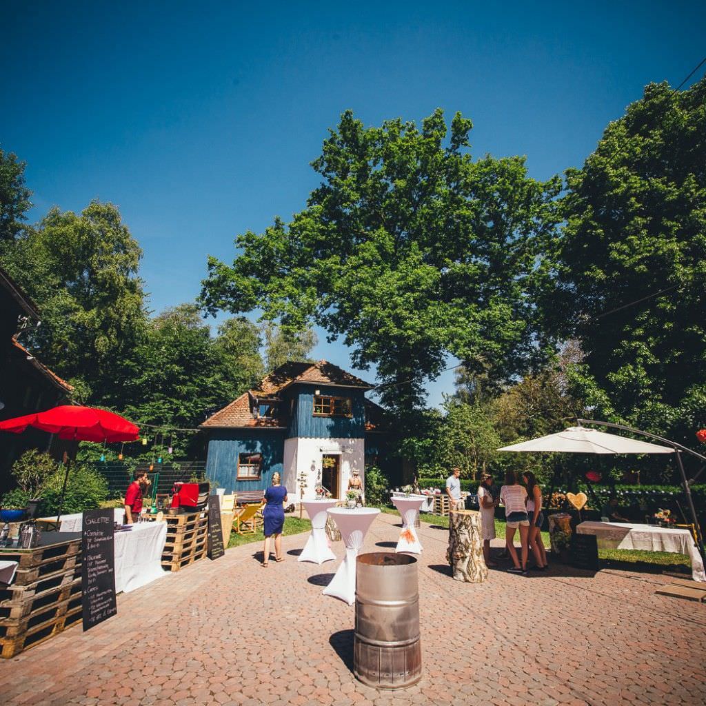 Entspannte Gäste bei einer rustikalen Sommerhochzeit draußen auf dem Bauernhof.