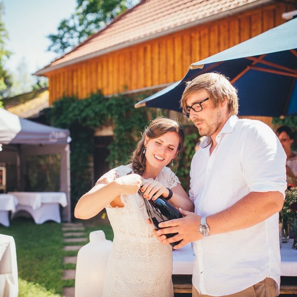 Brautpaar mit Sektflasche bei einer Sommerhochzeit auf dem Bauernhof.