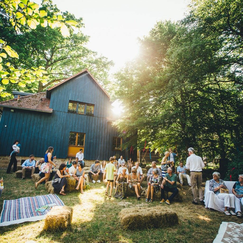 Entspannte Gäste bei einer rustikalen Sommerhochzeit draußen auf dem Bauernhof.