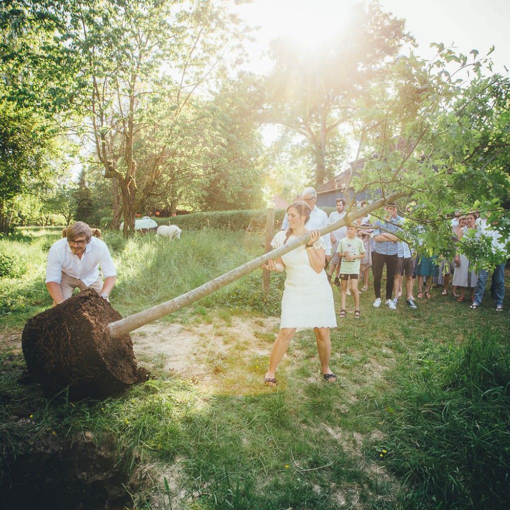 Das Brautpaar pflanzt bei ihrer Sommerhochzeit auf dem Bauernhof einen Baum.