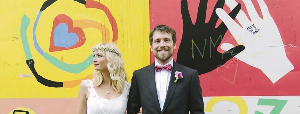 Das glückliche Hochzeitspaar posiert für Paarfotos vor einer bunt bemalten Wand.
