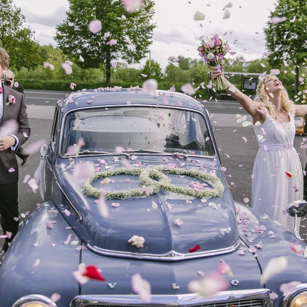 Das Braupaar mit dem Hochzeitsauto von Alter Schwede im Blütenregen.