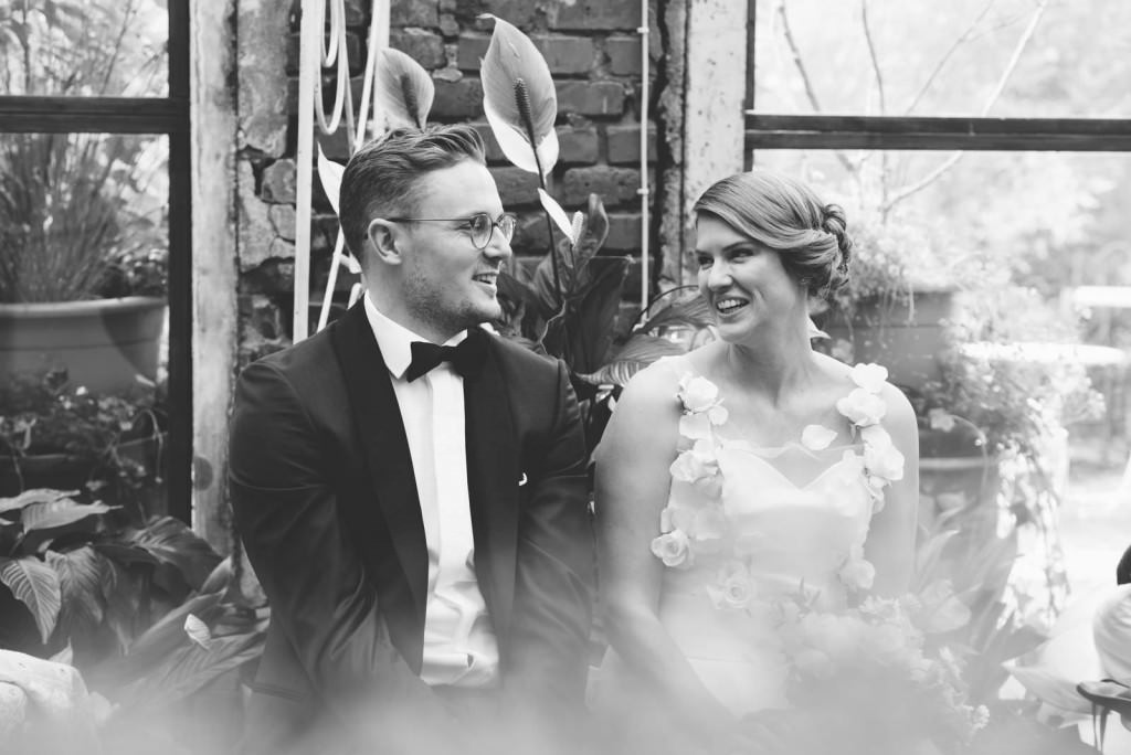 Paarfoto in schwarz-weiß: Das Brautpaar sitzt zwischen Blumen