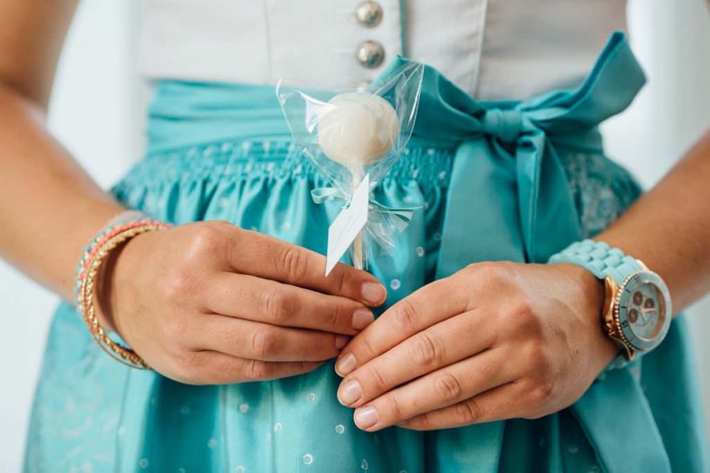 Brautjungfer in türkisfarbenem Dirndl mit Cake Pop in der Hand