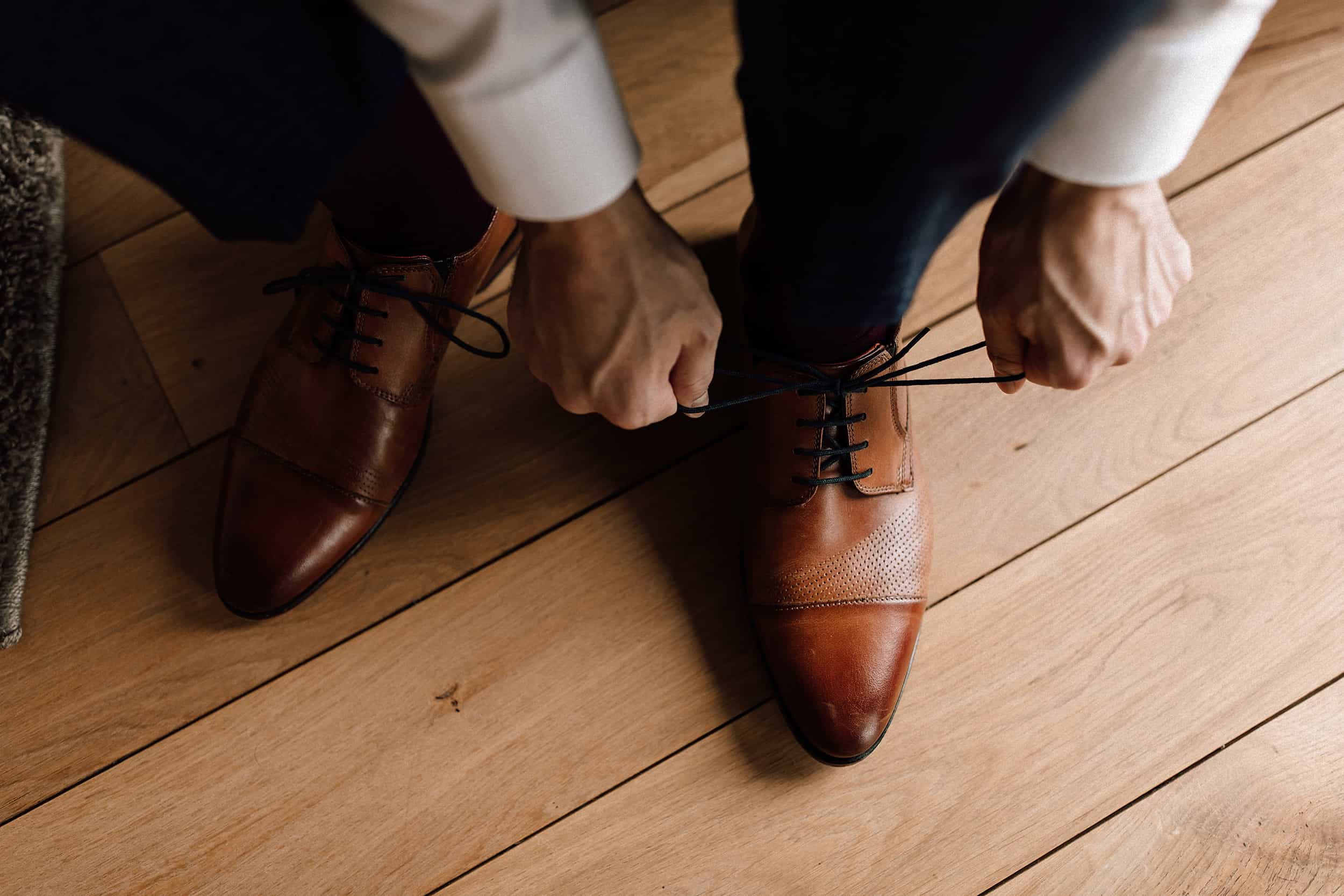Der Bräutigam bindet sich beim Getting Ready seine braunen Schuhe