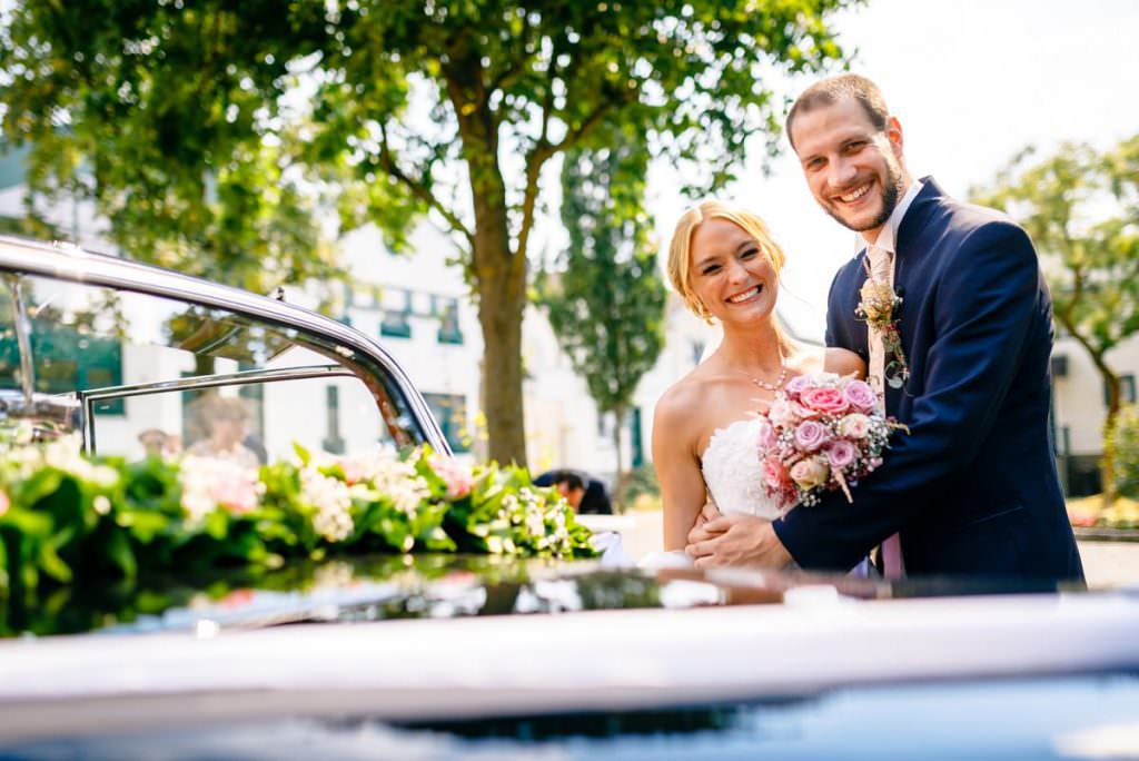 Paarfoto vom Brautpaar mit dem geschmückten Hochzeitsauto