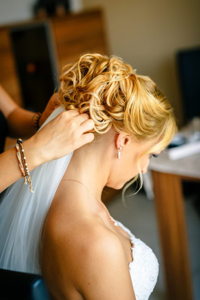 Hochzeitsfotoidee Getting Ready: Die Stylistin steckt der Braut den Schleier an