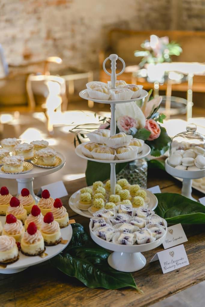 Hochzeits-Kuchenbuffet mit weißen Etageren und Kuchenplatten mit Törtchen und kleinen Kuchen