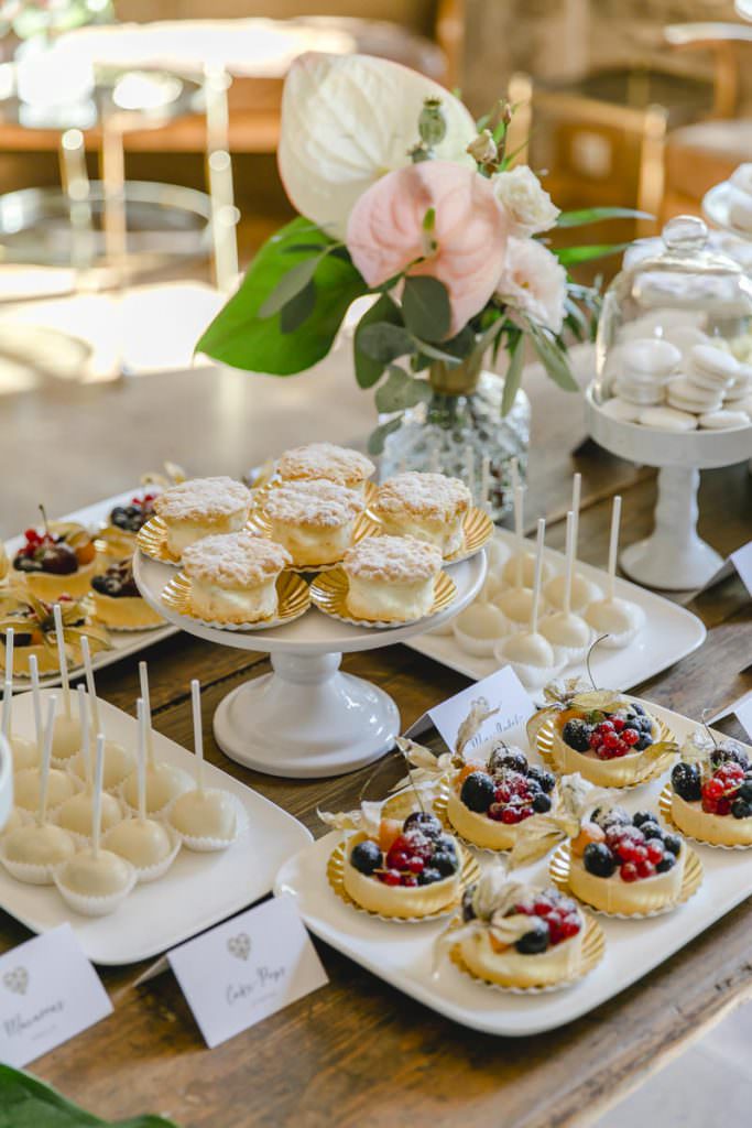 Törtchen mit Obst und Creme, weiße Cake Pops und Macarons auf dem Sweet Table einer Hochzeit