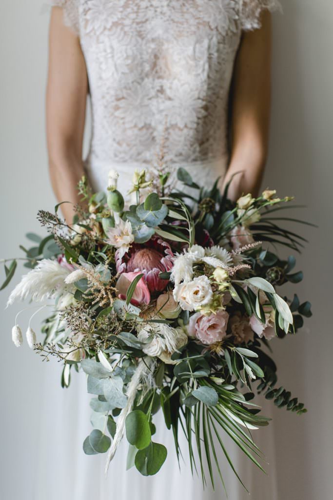 moderner Boho Brautstrauß mit pinkfarbener Protea, Pampasgras, Eukalyptus und Blumen in Rosa und Weiß