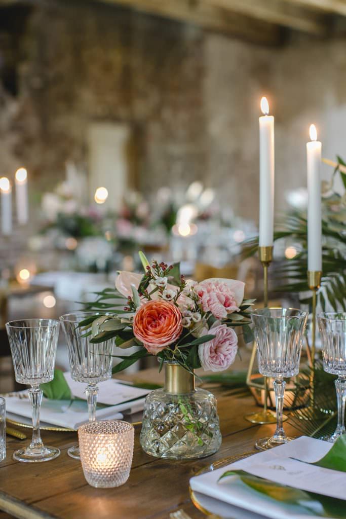 Hochzeitstischdeko mit goldenen Kerzenleuchtern, Kristallgläsern und Blumen in Rosa und Weiß.