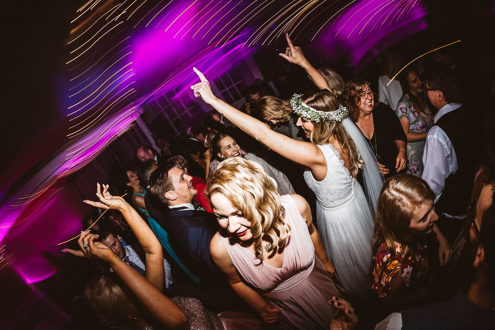 Tanzende Hochzeitsgäste unter pinkfarbenem Diskolicht recken die Hände in die Höhe.