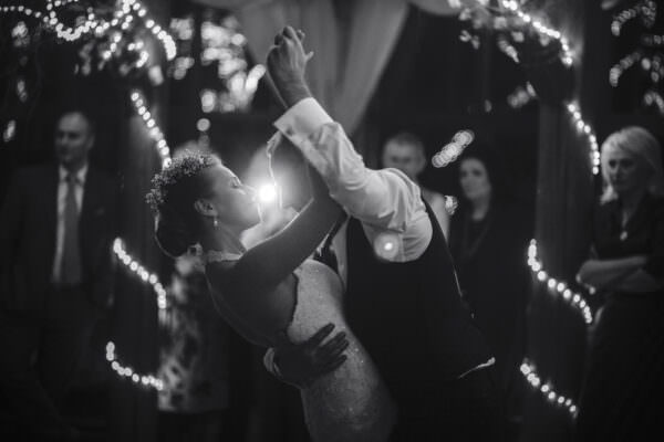 Schwarz-Weissfoto mit einem tanzenden Hochzeitspaar. Im Hintergrund glitzernde Lichterketten.