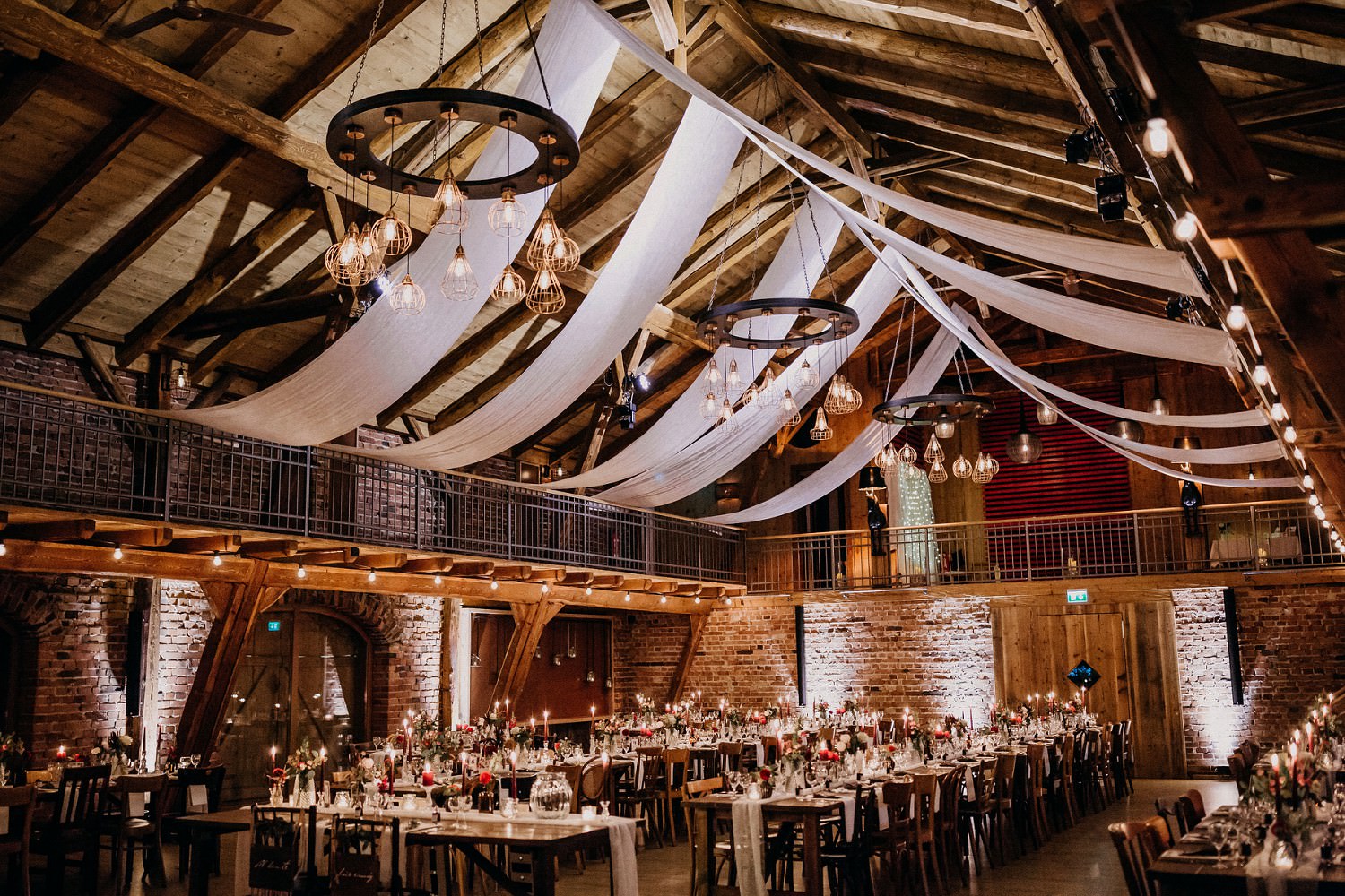 Scheunenhochzeit auf Hof Frien mit langen Hochzeitstafeln, vielen Lichtern und Kronleuchtern unter der Decke