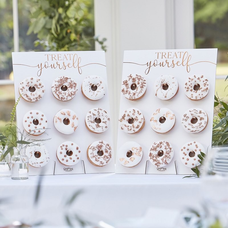 Weisse Donuts in Dreierreihen auf eine Pappe gespiesst. Darüber die Aufschrift „Treat yourself“.