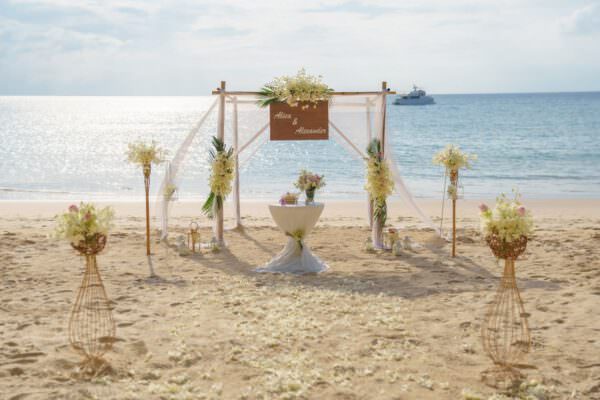 Ein Aufbau für eine Hochzeit in Thailand am Strand. Vorne ist ein Bambustor zusehen mit einem Schild. Gleich dahinter ist das Meer.